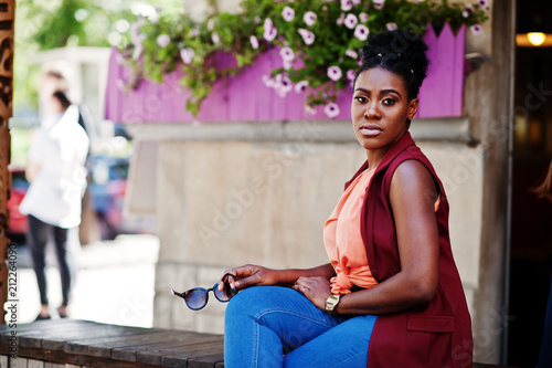 African american girl sitting outdoor with sunglasses at hands. photo