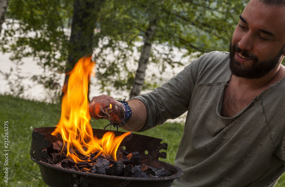 hipster mann entzündet holzkohle auf seinem grill. eine grosse stichflamme  erwärmt sein hand. Stock Photo | Adobe Stock