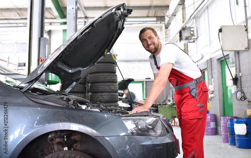 fröhlicher KFZ Mechaniker in einer Werkstatt bei der Autoreparatur // cheerful car mechanic in a workshop during car repair