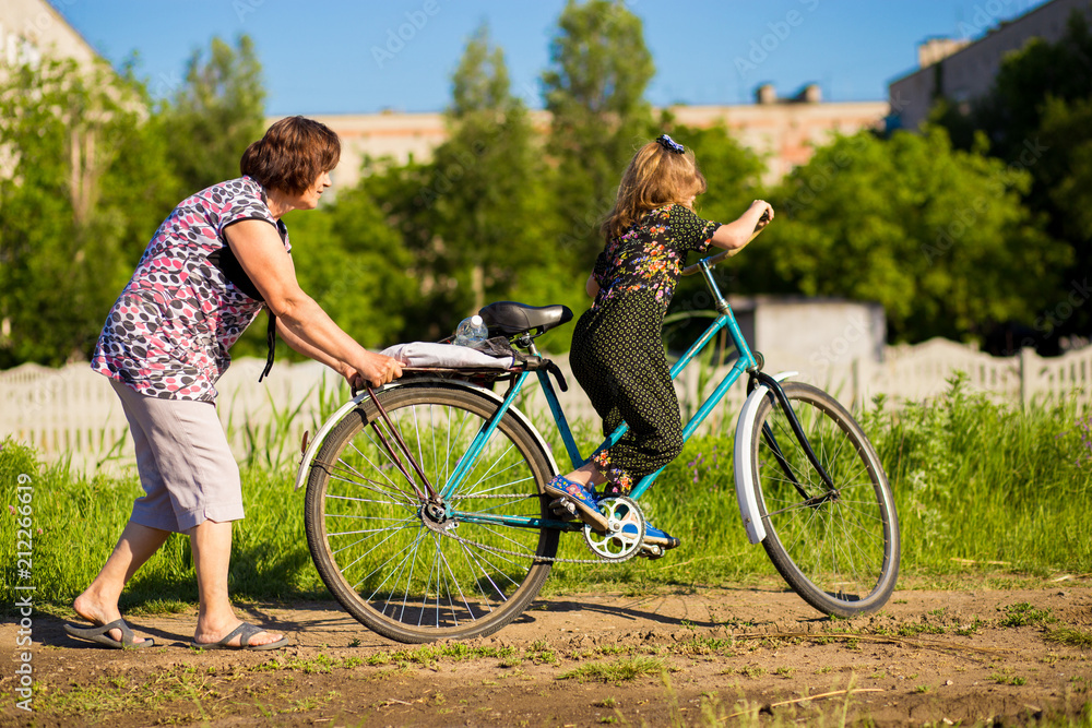 Obraz premium Grandmother teaches little granddaughter to ride old big bike