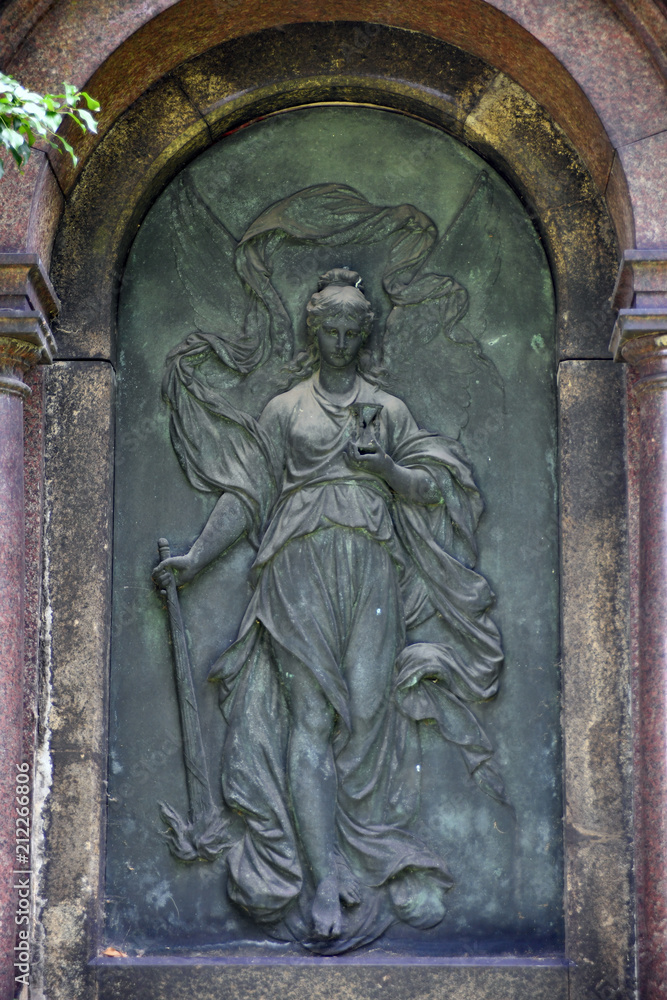 A weathered relief of an angel who walks forward, the relief is placed in front of a crypt.