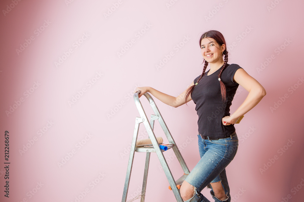 Picture of cheerful woman with brush next to stepladder and roller against blank pink wall