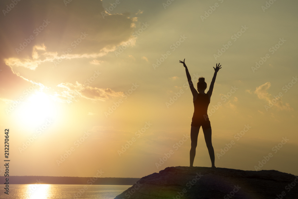 girl at the top of the mountain, raising her hands up against the sunset. Concept of sport, yoga, relaxation, meditation.