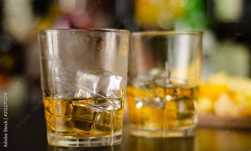 glass of whiskey with ice cubes and salty snacks on the background of bottles and bar glass of whiskey with ice cubes and salty snacks on the background of bottles and bar