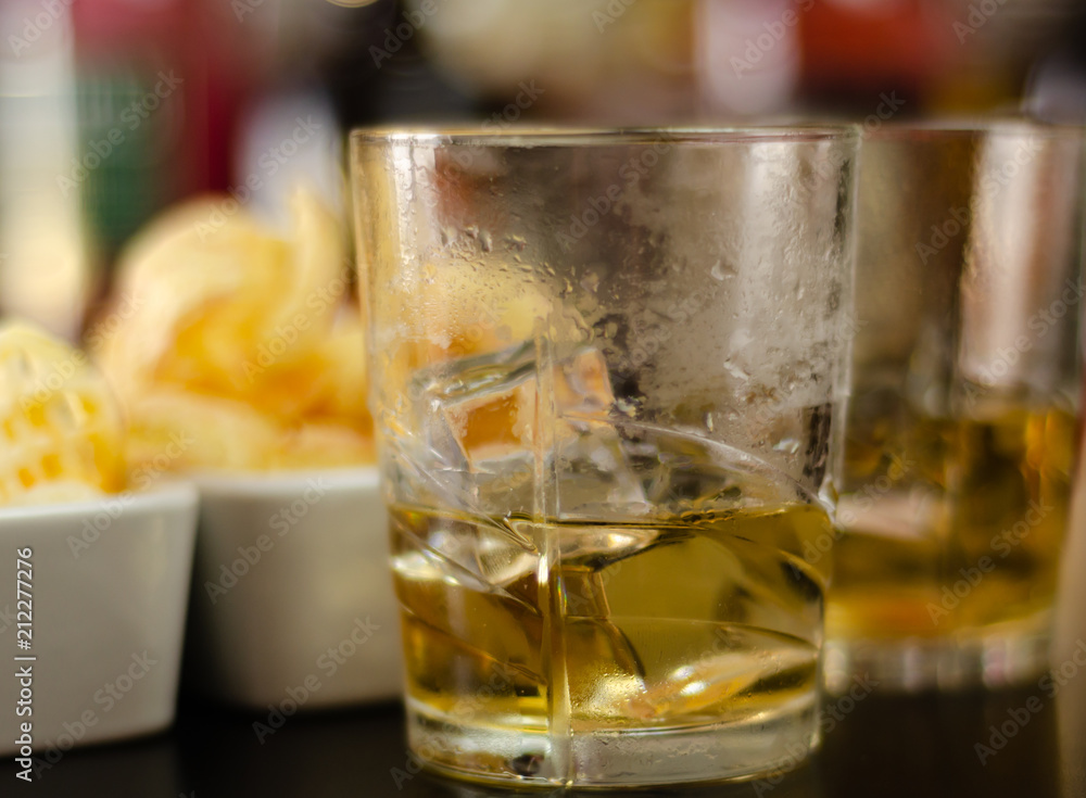 glass of whiskey with ice cubes and salty snacks on the background of bottles and bar glass of whiskey with ice cubes and salty snacks on the background of bottles and bar