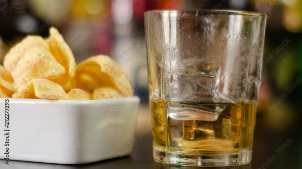 glass of whiskey with ice cubes and salty snacks on the background of bottles and bar glass of whiskey with ice cubes and salty snacks on the background of bottles and bar