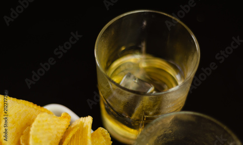 glass of whiskey with ice cubes and salty snacks on a black background