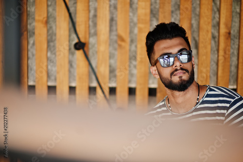 Handsome tall arabian beard man model at stripped shirt posed outdoor. Fashionable arab guy at sunglasses.