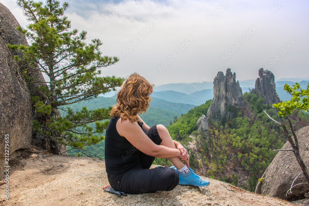On a mountaintop/ Young female rock climber meditating on top of a mountain. In the background are visible bizarre rocks called 