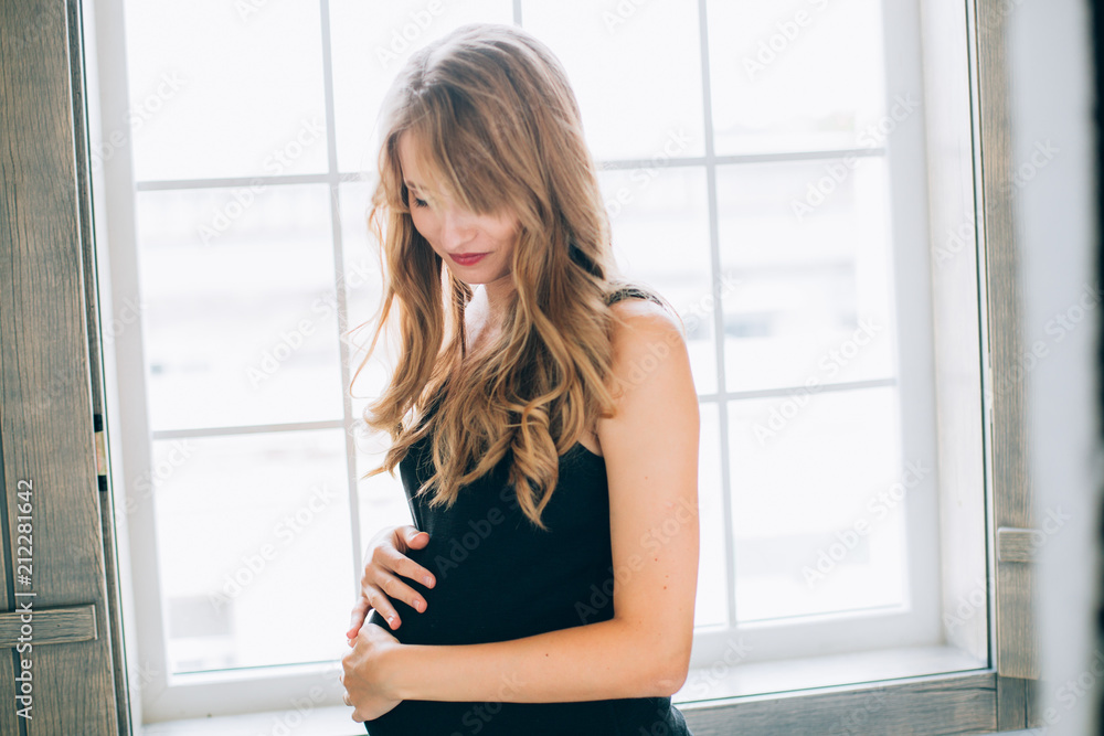 Beautiful young pregnant woman with long hair posing at home against window .. Beautiful young pregnant woman with long hair posing at home against window ..