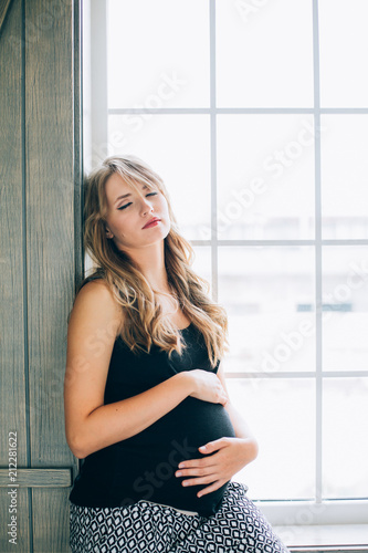 Beautiful young pregnant woman with long hair posing at home against window ..