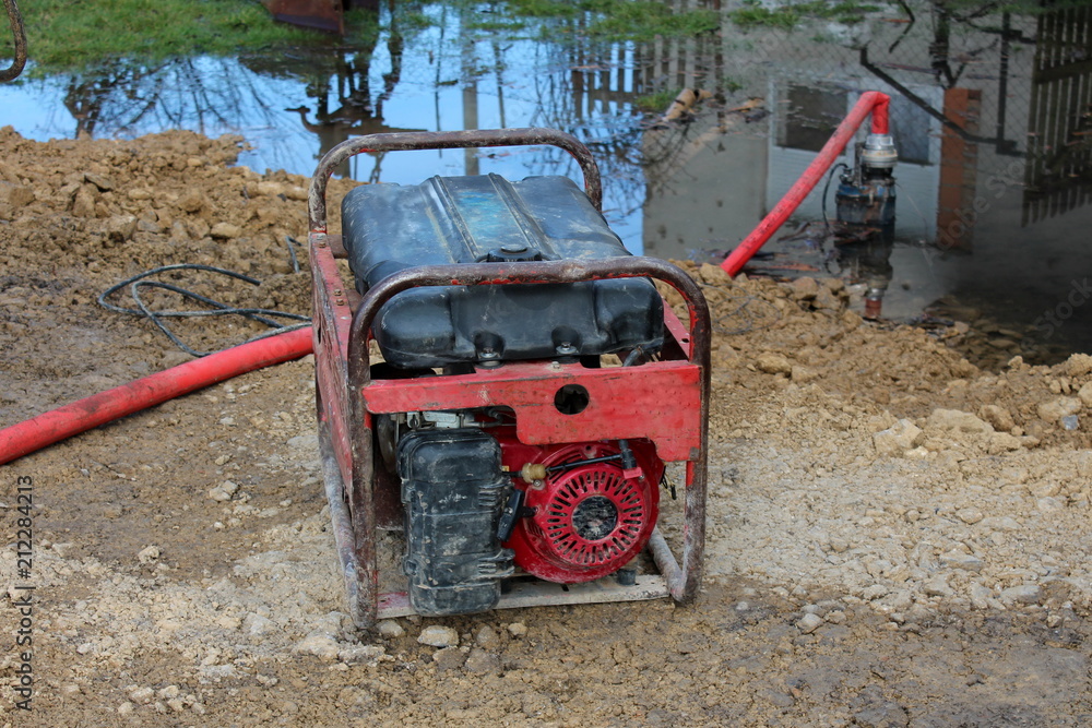 Petrol water pump with hard metal frame pumping water from side of the road using large red hose