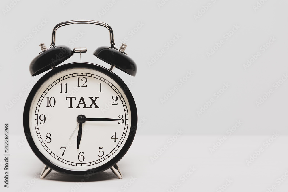 A black clock on light color background. Tax time alert. A black clock on light color background. Tax time alert.