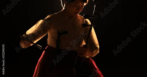 Korean female musician playing the Haegeum which is the Korean traditional string instrument on stage with spotlight photo