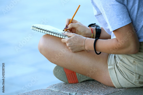 girl draws in a notebook sitting on the pavement