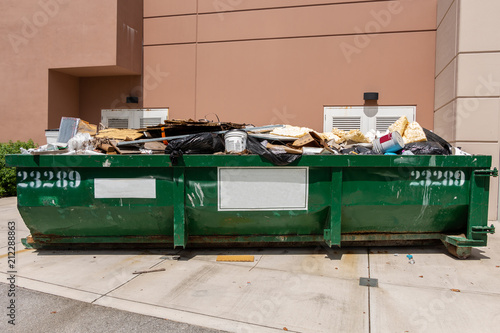 Large green metal dumpster filled with garbage from building renovation - Fort Lauderdale, Florida, USA