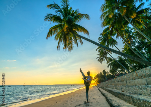 Mui Ne, Vietnam - April 21, 2018: Woman performing yoga exercises workout on the beach in the afternoon sunset beside palm trees, beautiful paradise beach in Mui Ne, Vietnam © huythoai