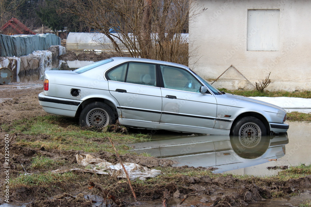 Car left in backyard during flood with water rising and front part already in water with large sandbox barriers used for flood protection in background