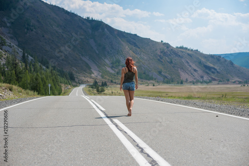girl with red hair walking on a mountain road alone. woman walking alone on empty mountain road