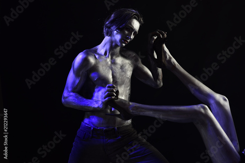 Dominating concept. man dominating woman holding her silver legs on black background