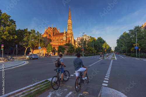 Two cyclists riding in bike lane in Barcelona street with a church on the background
