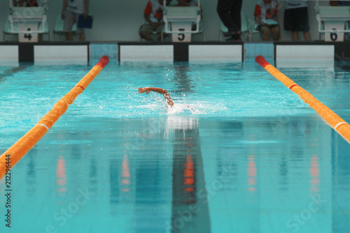 Young swimmer with white swimming cap swims front crawl or forward crawl in the swimming pool for competition