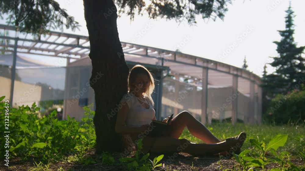 Caucasian girl student sitting under the tree and reading a book at summer sunset Caucasian girl student sitting under the tree and reading a book at summer sunset