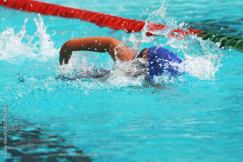 Young man swimmer with blue cap swims front crawl or forward crawl stroke in a swimming pool for competition or race
