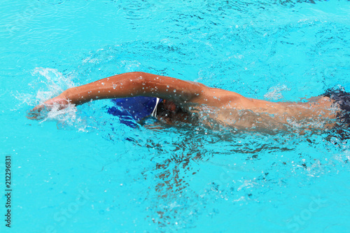 Young man swimmer with blue cap swims front crawl or forward crawl stroke in a swimming pool for competition or race
