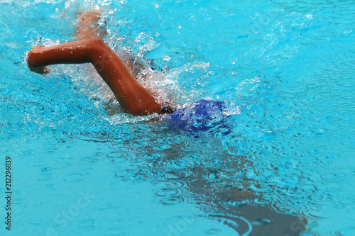 Young man swimmer with blue cap swims front crawl or forward crawl stroke in a swimming pool for competition or race