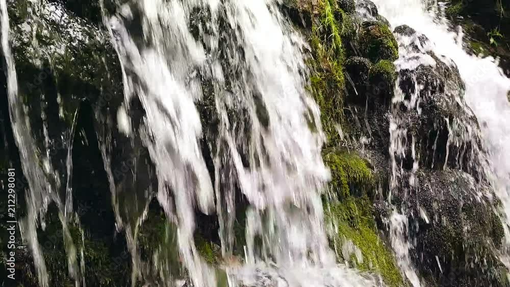 Slow motion of a small mountain waterfall. The mountain stream falls down on stones in a bottom. Slow motion of a small mountain waterfall. The mountain stream falls down on stones in a bottom.
