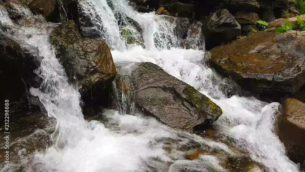 Slow motion of a small mountain waterfall. The mountain stream falls down on stones in a bottom. Slow motion of a small mountain waterfall. The mountain stream falls down on stones in a bottom.