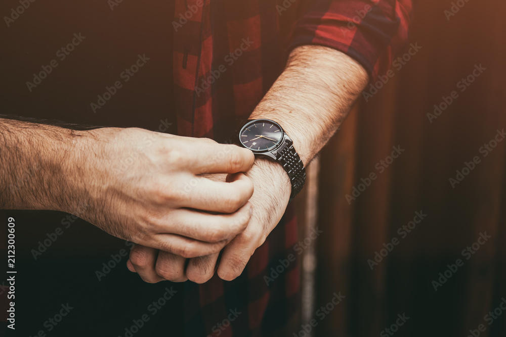 young fashionable man wearing a black analog wrist watch. street style detail of an elegant clock. vintage faded grade
