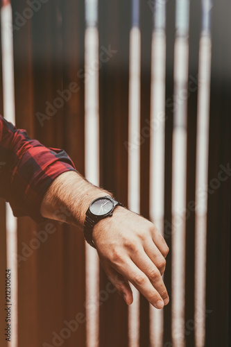 young fashionable man wearing a black analog wrist watch. street style detail of an elegant clock. vintage faded grade