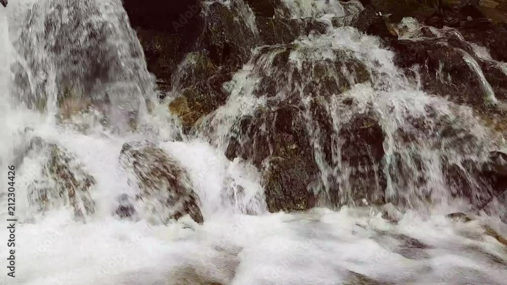 Slow motion of a small mountain waterfall. The mountain stream falls down on stones in a bottom. Slow motion of a small mountain waterfall. The mountain stream falls down on stones in a bottom.