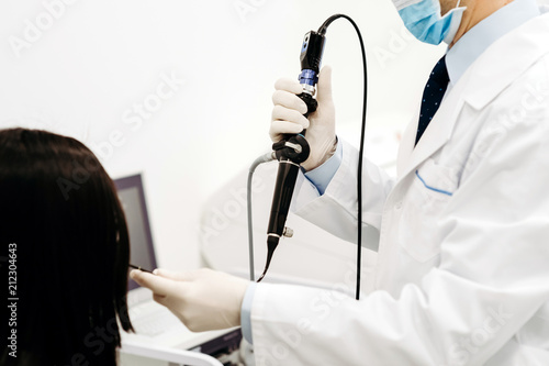 The otolorinologist conducts manipulations to investigate the diseases of the nose with the help of endoscope and a probe. Hands in gloves, on the head a sterile mask and a doctor's medical flashlight