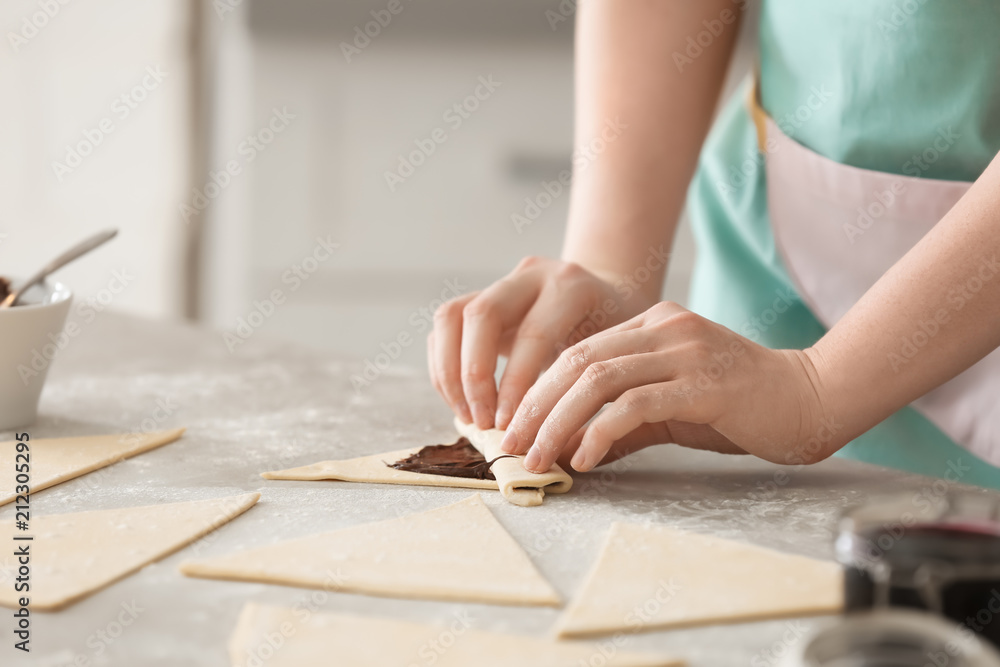 Woman preparing tasty croissants with chocolate paste on table, closeup