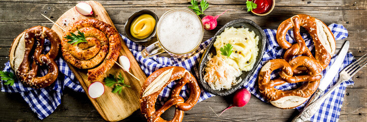 Oktoberfest food menu, bavarian sausages with pretzels, mashed potato, sauerkraut, beer bottle and mug old rustic wooden background, copy space above banner format