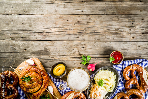 Oktoberfest food menu, bavarian sausages with pretzels, mashed potato, sauerkraut, beer bottle and mug old rustic wooden background, copy space above