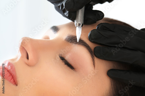 Young woman undergoing procedure of eyebrow permanent makeup in beauty salon, closeup