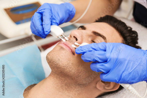 Young man undergoing microcurrent therapy in beauty salon  closeup