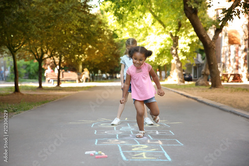 Little children playing hopscotch drawn with colorful chalk on asphalt