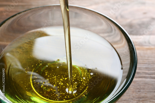 Pouring fresh olive oil into bowl on wooden background, closeup