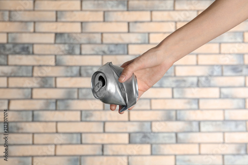 Woman holding crumpled aluminum can on brick wall background. Metal waste recycling