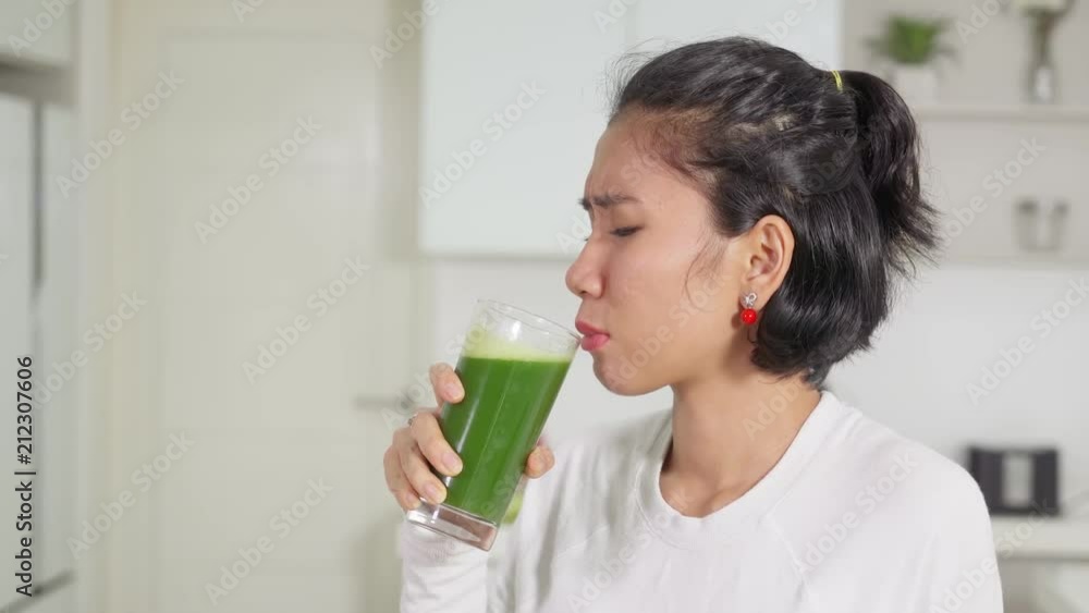 Young woman drinking a glass of vegetables juice with dislike expression in the kitchen at home. Shot in 4k resolution Young woman drinking a glass of vegetables juice with dislike expression in the kitchen at home. Shot in 4k resolution