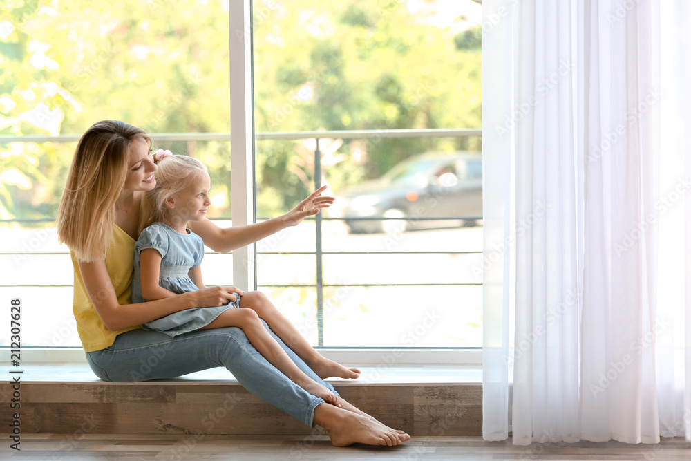 Young woman with cute little girl near window at home Young woman with cute little girl near window at home