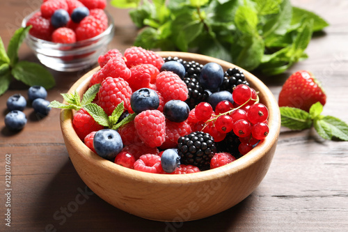 Bowl with raspberries and different berries on wooden table