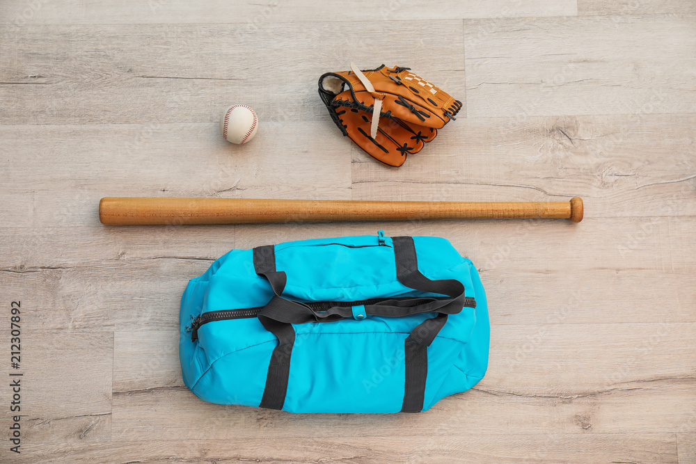 Sports bag, baseball ball and bat on wooden floor, top view