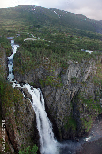 A tall beautiful waterfall falls into a dark gorge, at the top are low mountains