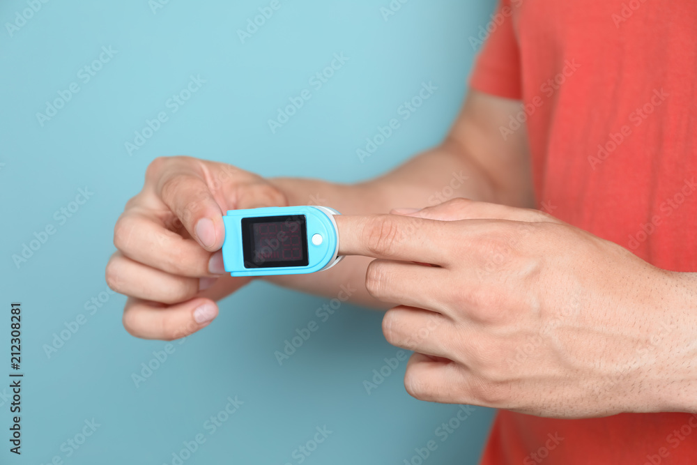 Young man checking pulse with blood pressure monitor on finger against color background, closeup Young man checking pulse with blood pressure monitor on finger against color background, closeup